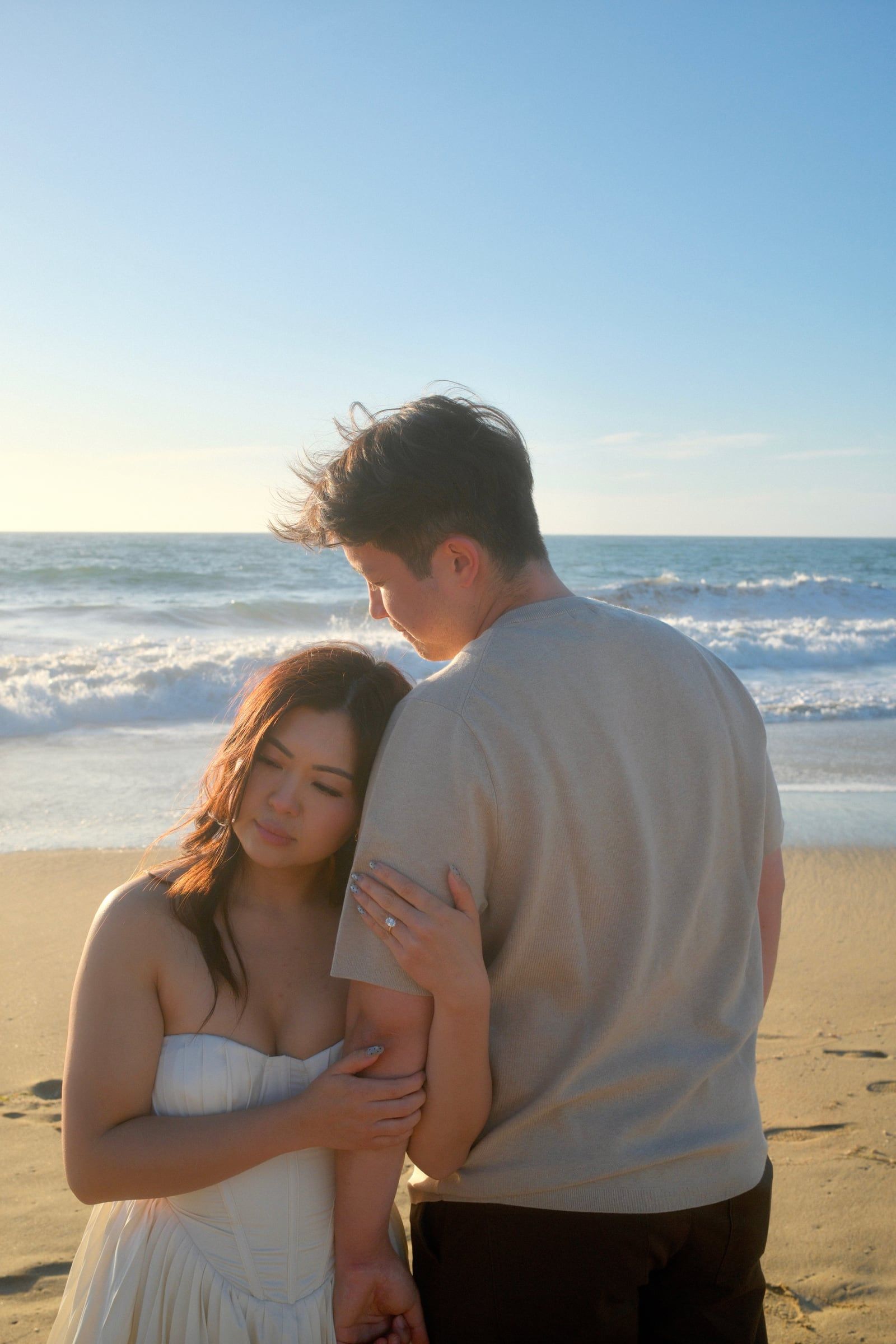 Julie resting her head on Matthew's arm on the beach, waves behind them