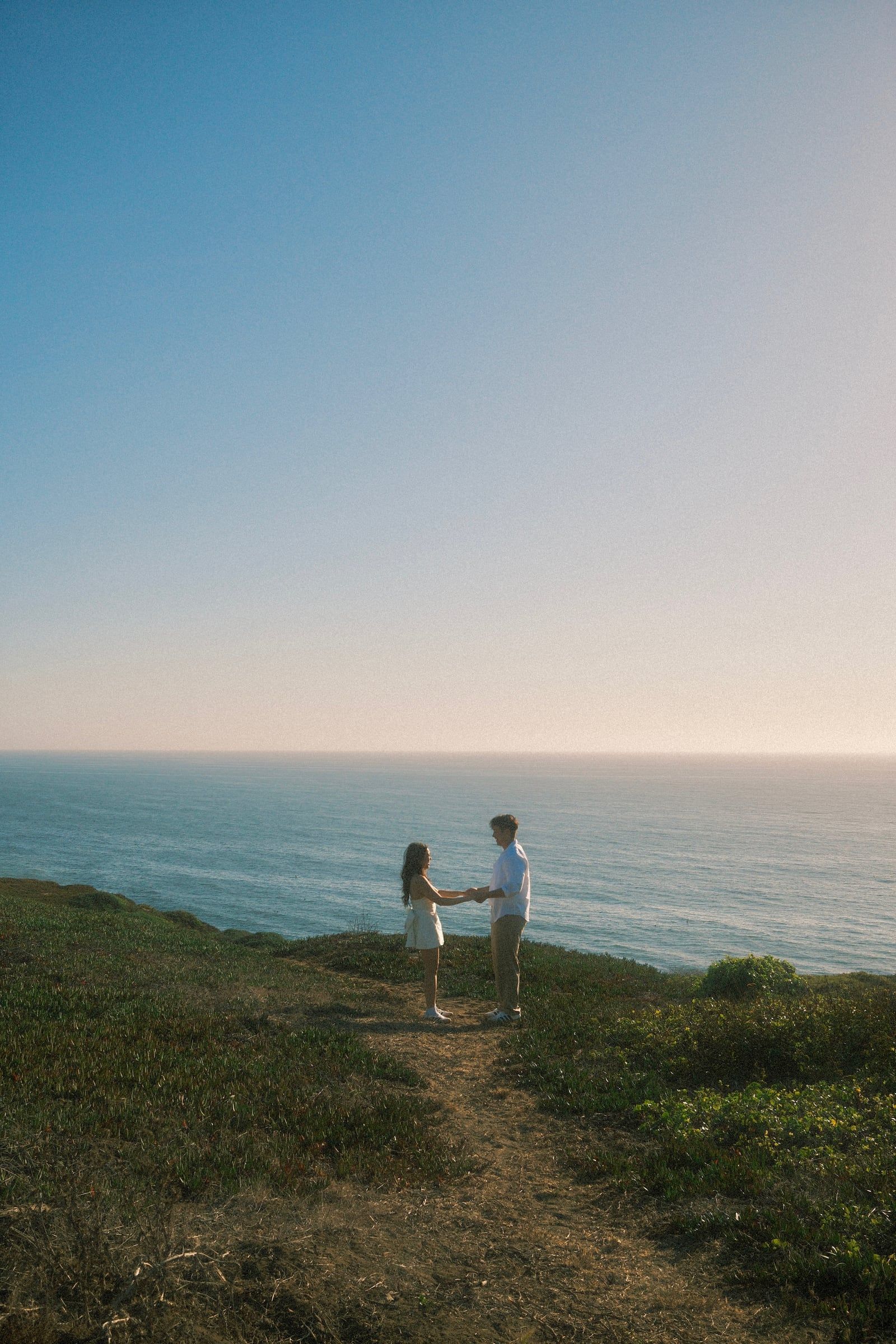 Matthew and Julie holding hands on a clifftop path above the ocean