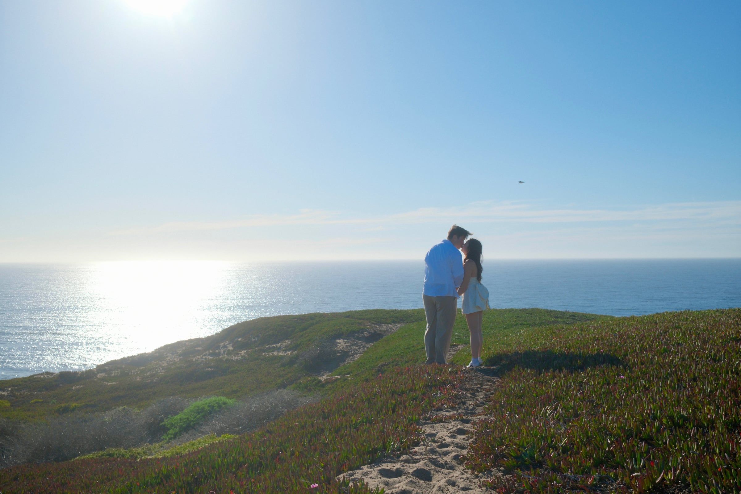 Matthew and Julie kissing on a clifftop trail above the ocean