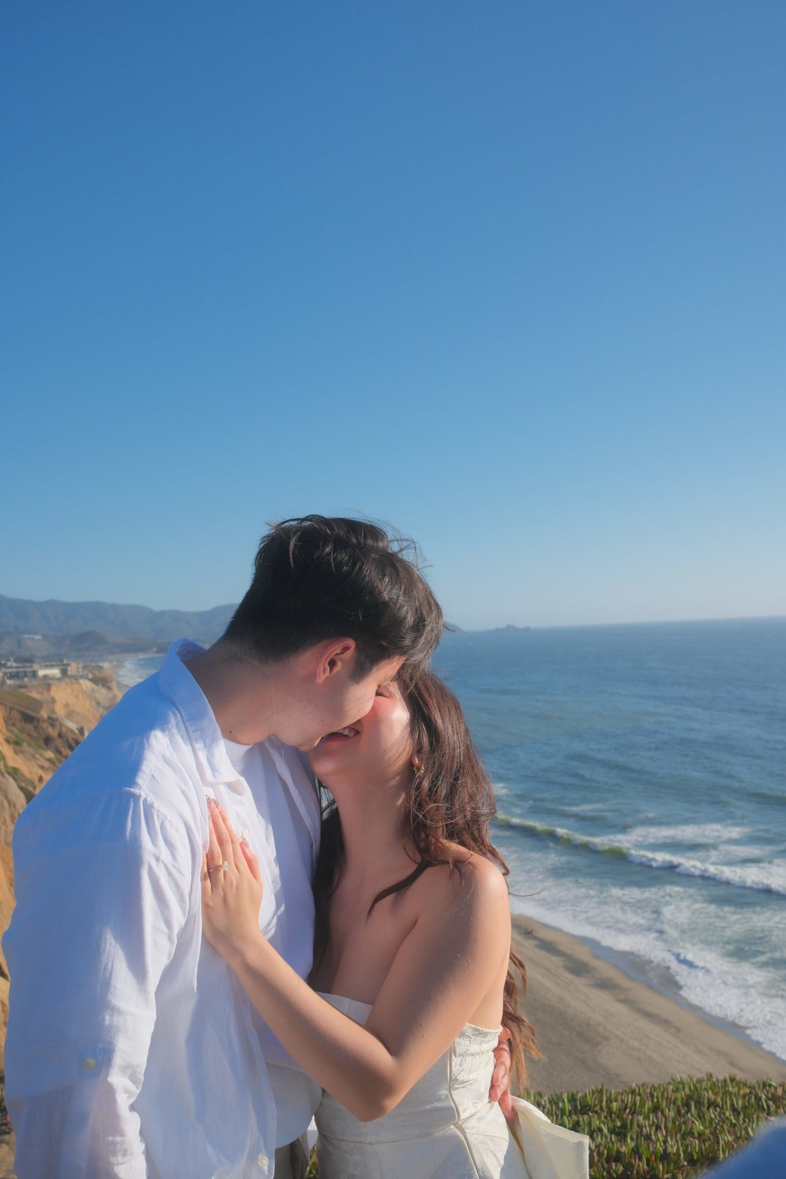 Matthew kissing a laughing Julie on the bluffs, the coastline stretching behind them