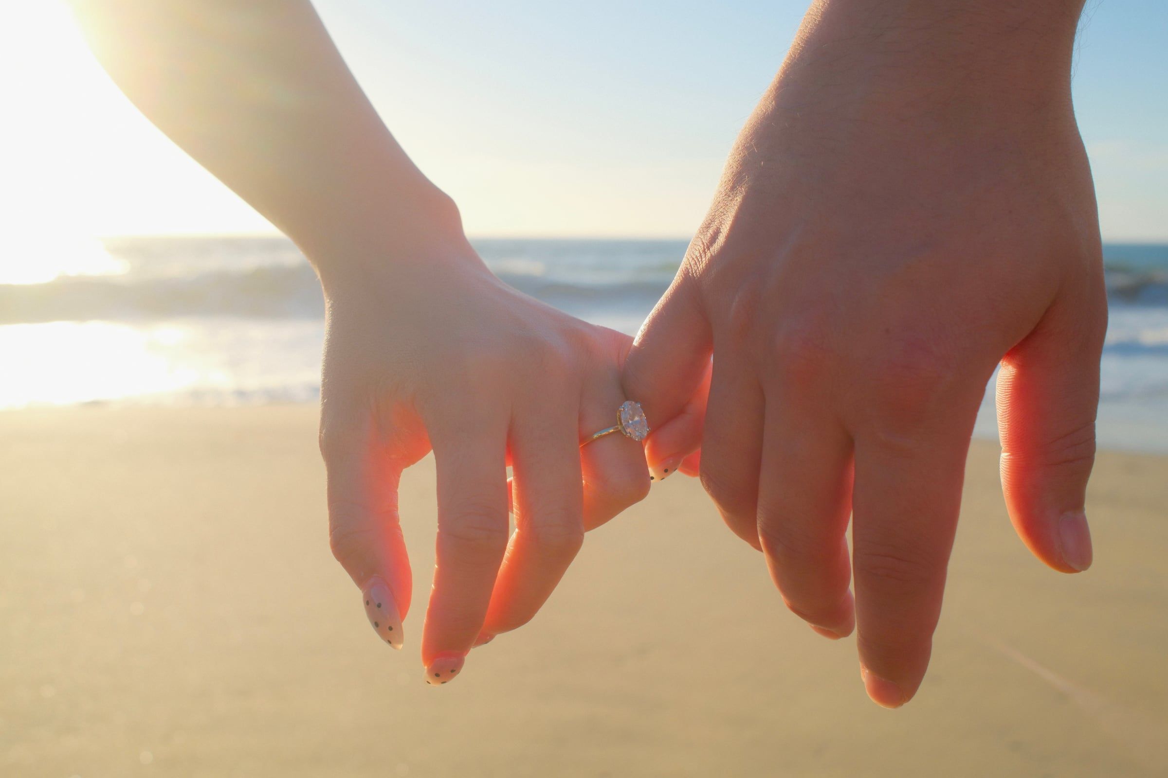 Matthew and Julie's hands linked by the pinky, her engagement ring catching the sun